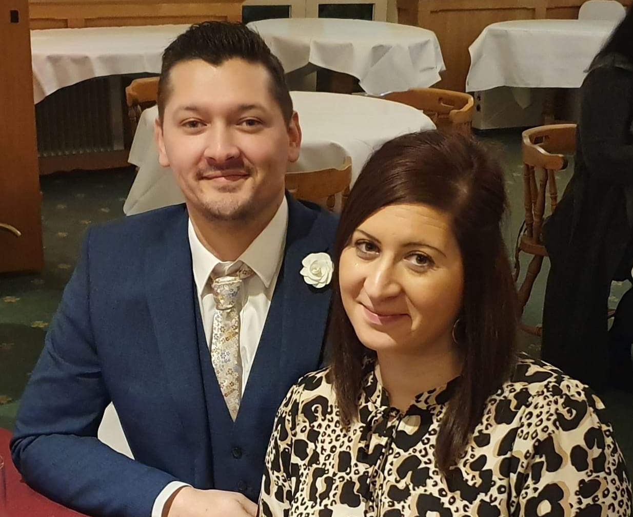 Craig and Fariba Foster. Craig is on the let in a blue suit, Fariba is on the right in a patterned shirt. They are both smiling.