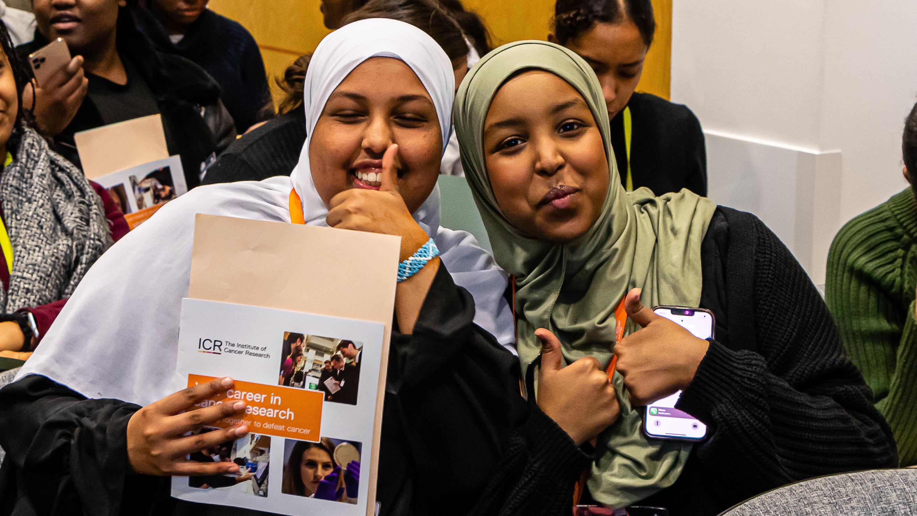 Two girls smiling and holding their thumbs up with a careers booklet