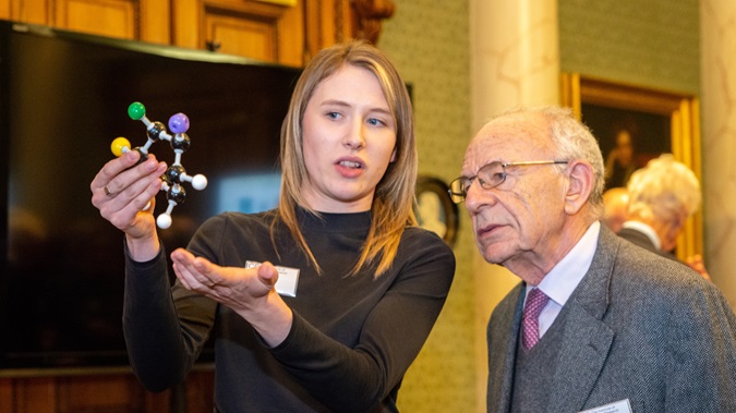 Discovery club - A young woman in black and an older man in a grey suit look at a molecule model