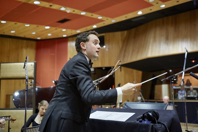 Philanthropy - finished symphony - a man wearing a black suit conducts an orchestra in a wooden panelled room