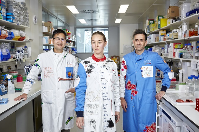 Philanthropy - lab coats - three scientists stand in an Institute of Cancer Research laboratory wearing lab coats covered in writing and pictures