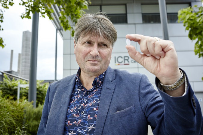 Philanthropy - poem on a pill - a man in a suit stands in front of the ICR's Centre for Cancer Drug Discovery holding a small pill in front of the sign