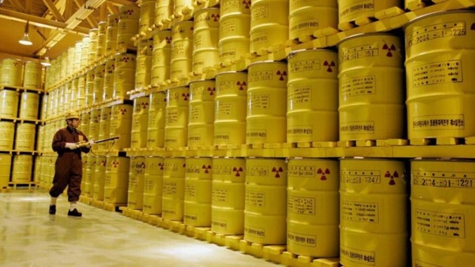 Waste adviser wearing protective uniform surveying barrels of radioactive waste