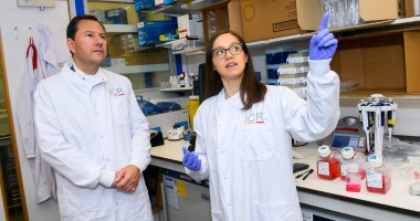 A man and a woman wearing lab coats look around a laboratory