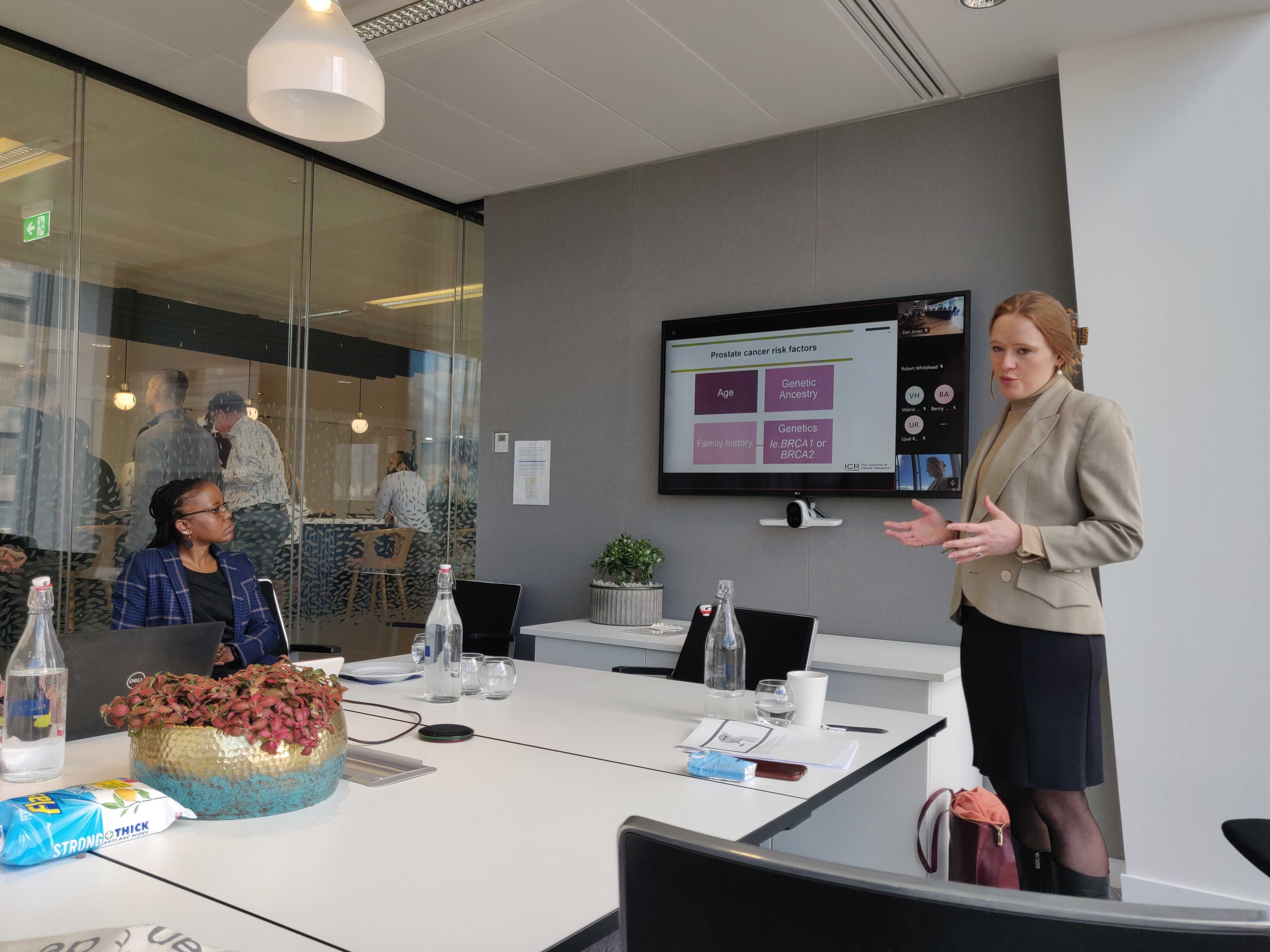 A woman in a suit jacket stands delivering a presentation in a meeting room