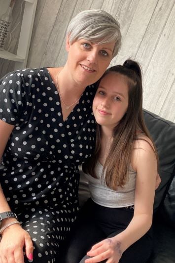 Caroline has her arm around her daughter Aleisha, both sitting on a sofa