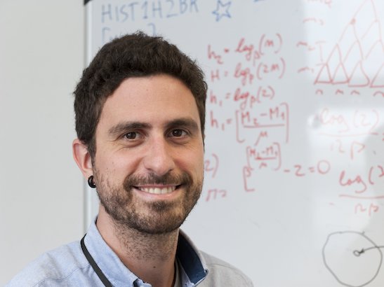 Dr Andrea Sottoriva in front of whiteboard with maths on it 547x410 Dr Andrea Sottoriva with whiteboard in background