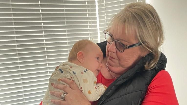 Glenys, cradles her newborn grandson Jacob and gazes down at him