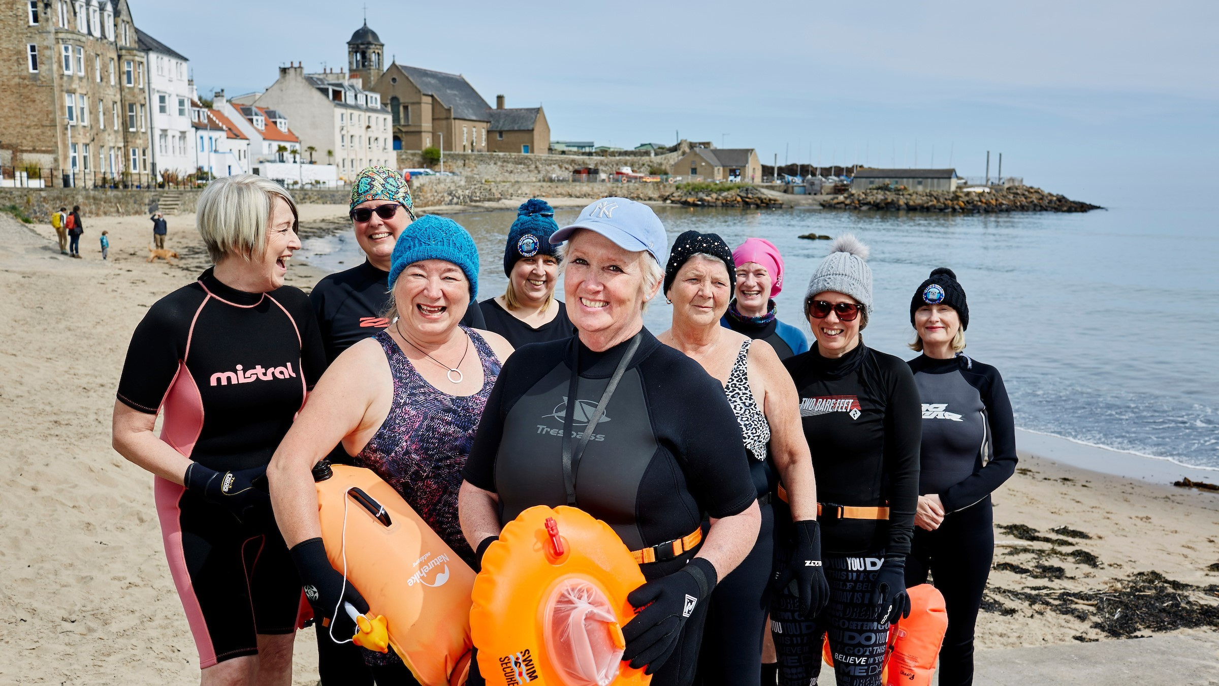 Karen holds a bright orange tow float surrounded by her swimming friends on the beach