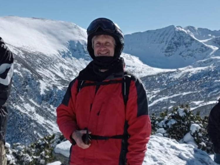 Mark is wearing ski gear and stands in front of a mountain