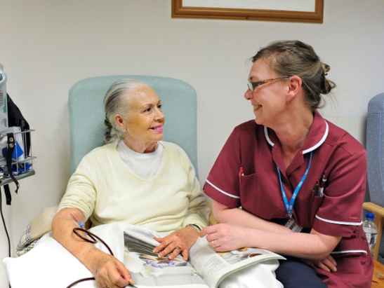 Elderly woman in hospital sitting down talking to a nurse