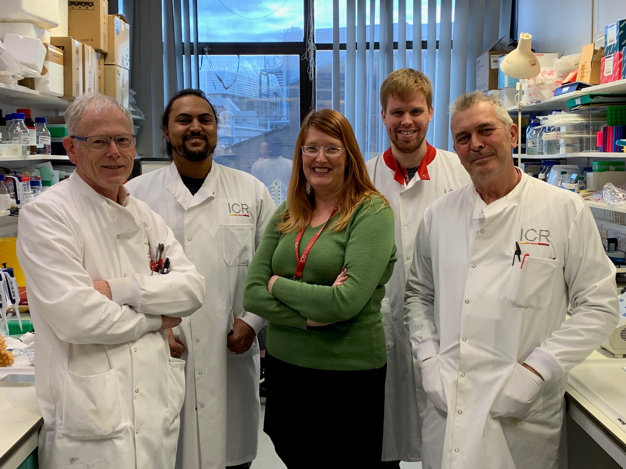 Five scientists in white coats pose for the camera in their laboratory