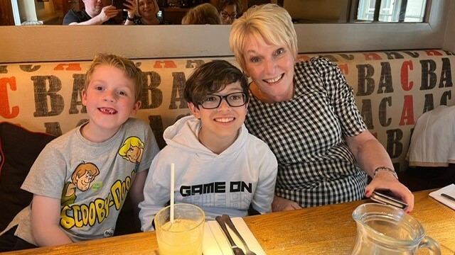 Sue sits with two young grandchildren at a restaurant, all smile at the camera