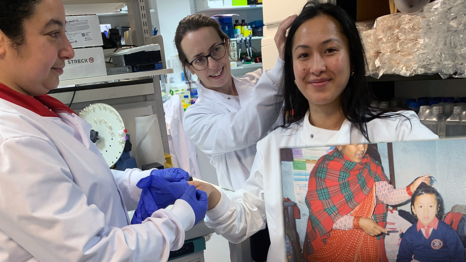 Sumana Shrestha in the lab holding up a printed picture of herself as a kid