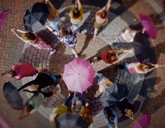 A still from the video We Dance for Life, showing a top down view of people twirling umbrellas which are also a creative interpretation of cancer cells